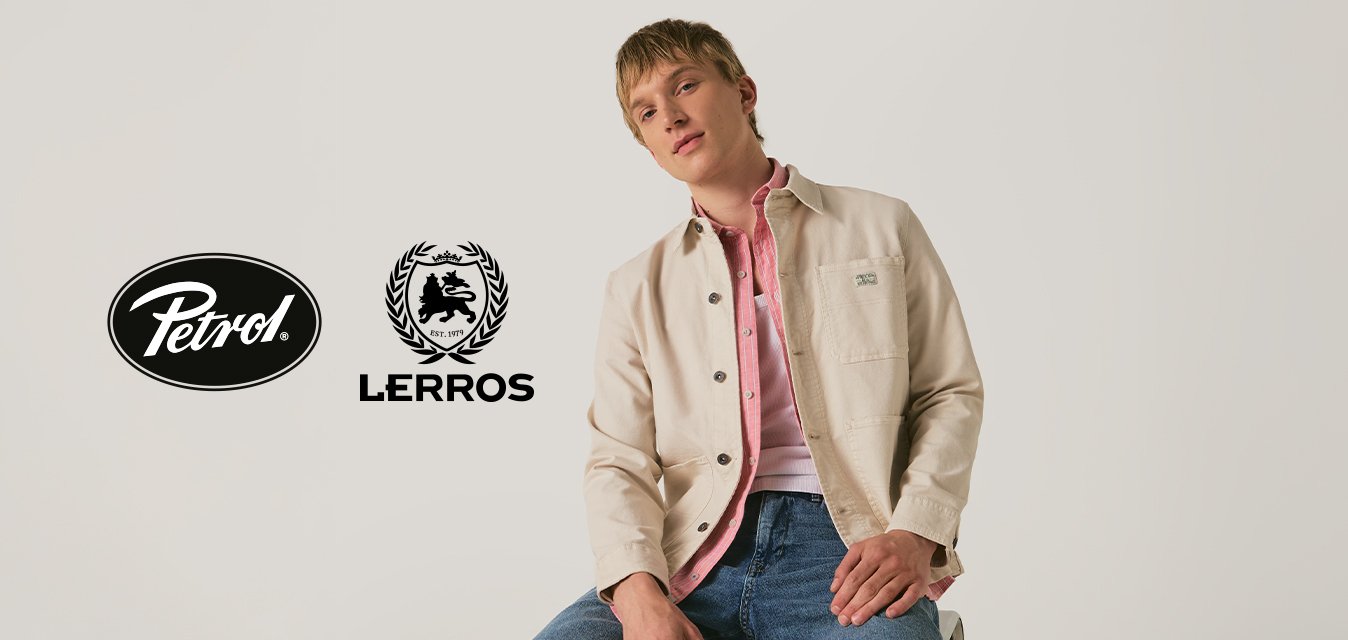 Junger Mann, der eine beige Jacke über einem rosa Hemd und blauen Jeans trägt, sitzt vor einem einfarbigen Hintergrund mit den Logos von Petrol und Lerros.