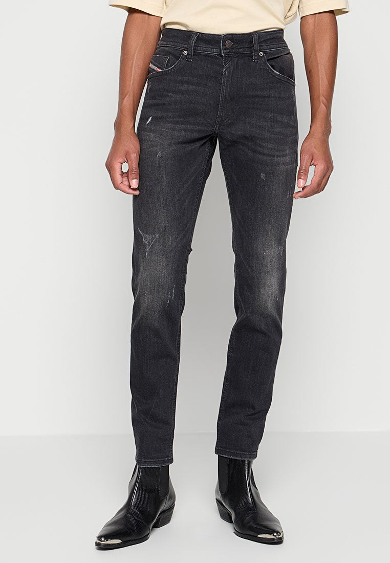 Schwarze Denim-Jeans mit Slim-Fit, ausgestattet mit abgenutzten Akzenten, fünf Taschen und einem kontrastierenden roten Etikett an der vorderen rechten Tasche.