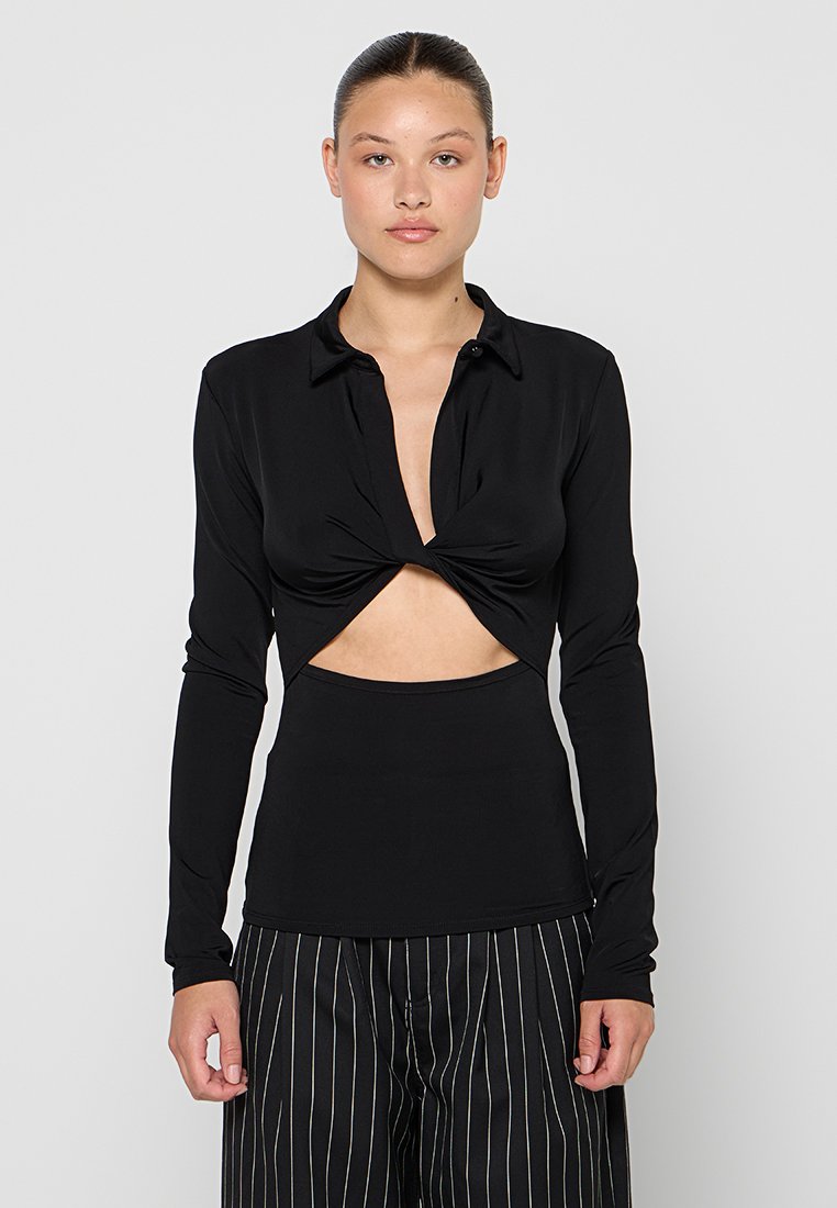 Schwarzes Langarmshirt mit Knotendesign auf der Vorderseite und einem Ausschnitt. Das Material wirkt glatt und hat eine figurnahe Silhouette sowie einen Kragen.