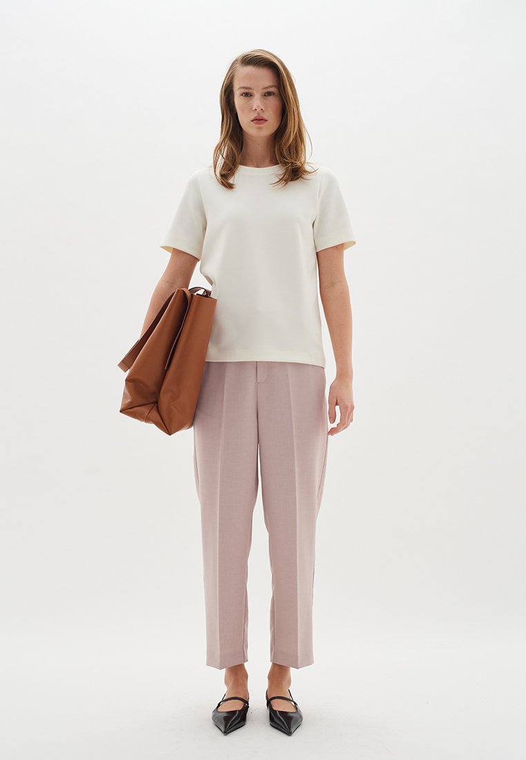 Weißes kurzärmliges Oberteil, hellrosa maßgeschneiderte Hose, schwarze spitze Ballerinas und eine große braune Lederhandtasche. Schlichtes, zeitgemäßes Design.