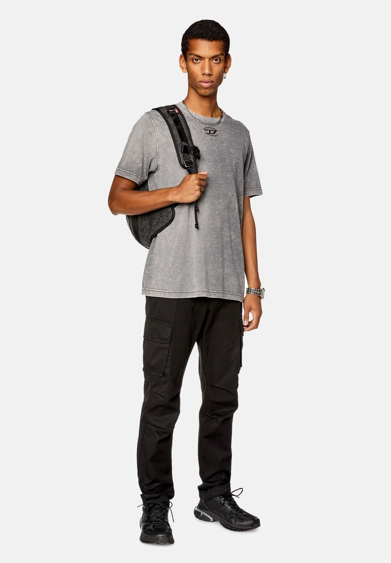 Graues, verblichenes T-Shirt mit lockerer Passform; schwarze Cargo-Hosen mit Taschen; schwarzer Rucksack; schwarze Sportschuhe mit strukturierten Sohlen; silberne Uhr.