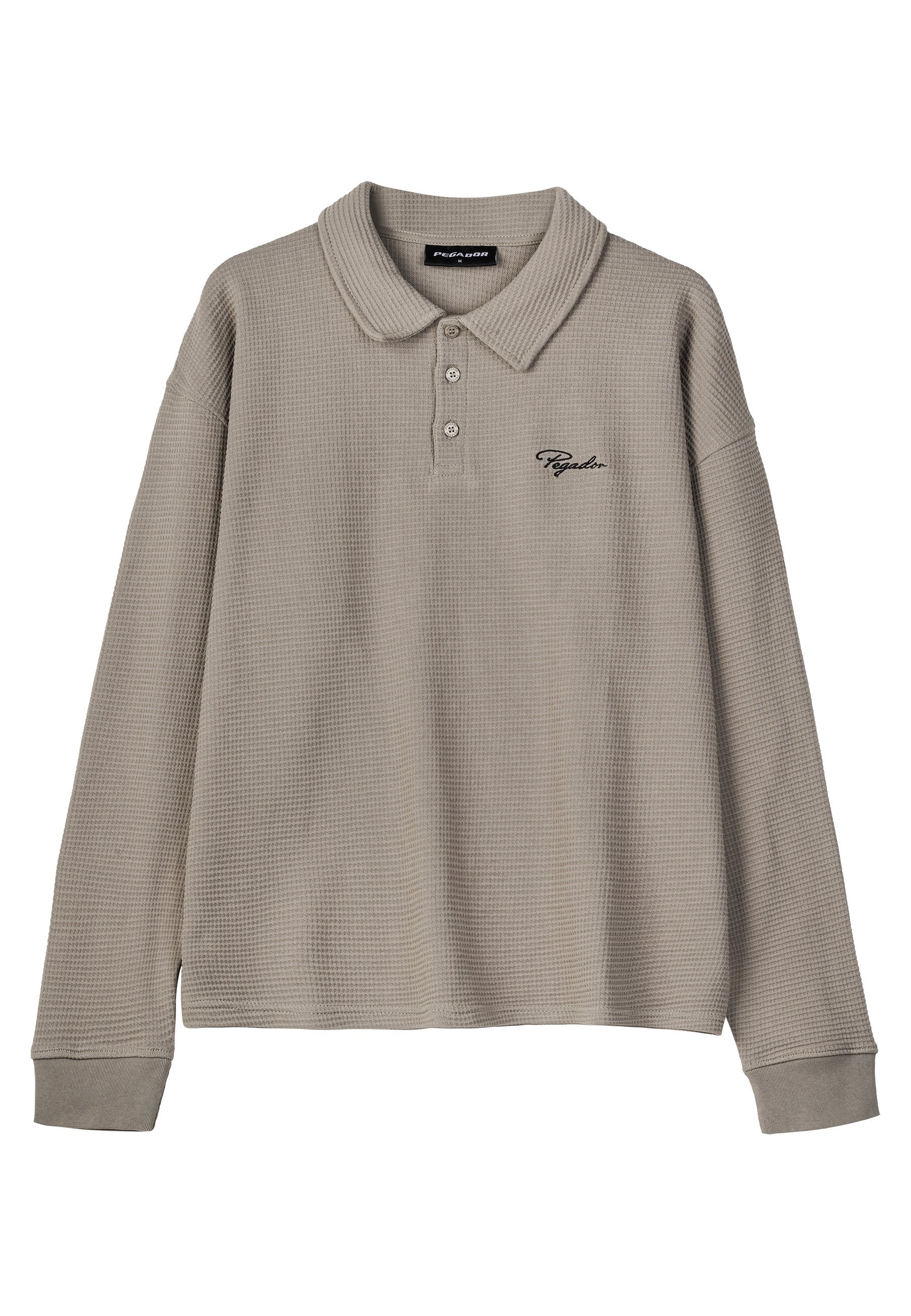 Helles graues Poloshirt mit Waffelstruktur und langen Ärmeln, mit drei Knöpfen und einem gerippten Kragen. Mit schwarzem gesticktem Logo auf der Brust.