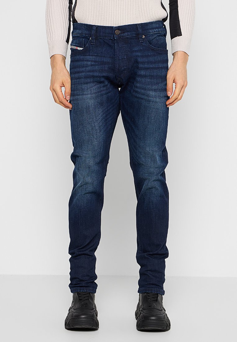 Dunkelblaue Jeans aus Denim, mit einer taillierten Passform, dezenten Verwaschungen und klassischem Fünf-Taschen-Design. Kombiniert mit schwarzen Sneakers.