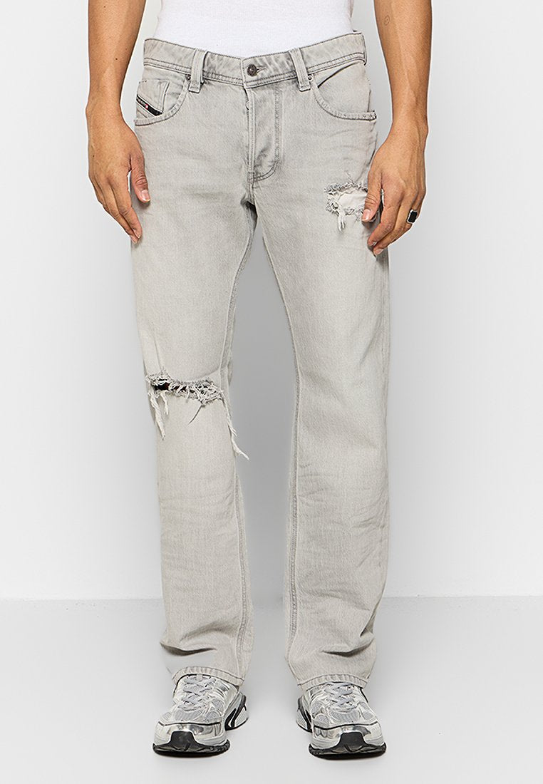 Hellgraue, ausgewaschene Jeans mit Rissen an den Knien, Fünf-Taschen-Design und einer leicht lockeren Passform, kombiniert mit grauen Sportschuhen.