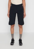 Person trägt schwarze knielange Shorts, graue Socken, schwarze und graue Sportschuhe, steht vor einem einfachen hellen Hintergrund.