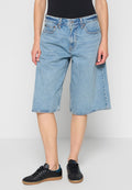 Hellblaue Denim-Shorts mit lockerem Schnitt, mittelhoher Taille und rohem Saum. Merkmale klassische Nähte und ein Design mit fünf Taschen. Getragen mit schwarzen Sneakern.