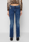 Frau in dunkelblauen geraden Jeans, braunem Leopardenmuster-Pullover in cropped Länge und schwarzen spitzen Stiefeln steht vor grauem Hintergrund.