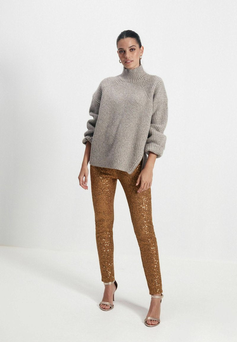Grauer, gerippter Rollkragenpullover mit langen, gepufften Ärmeln, kombiniert mit schmalen, glänzenden bronzefarbenen Pailletten-Hosen und metallischen, geschnürten High Heels.