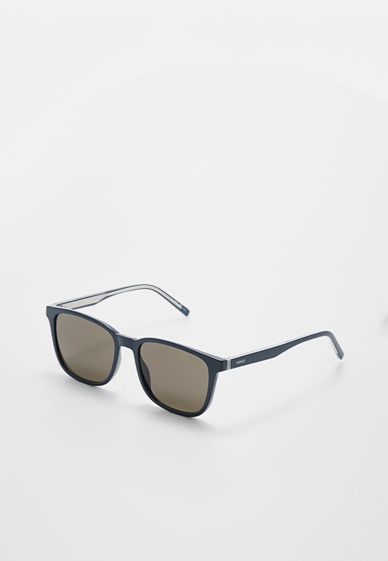 Schwarze rechteckige Sonnenbrille mit dunklen Gläsern und dünnen Bügeln, an der Seite mit "Hugo" gebrandet, auf einer weißen Oberfläche liegend.