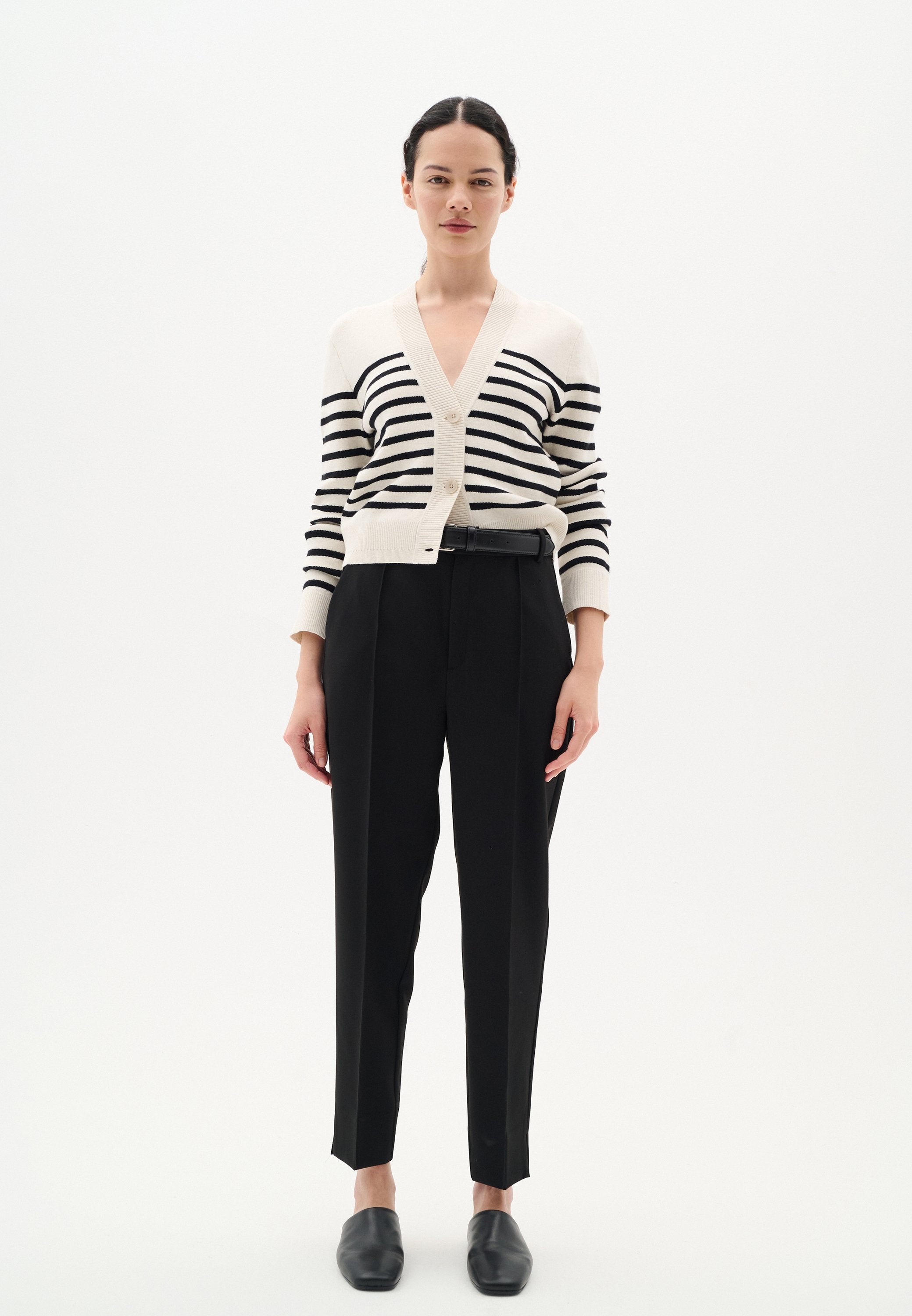 Gestreifter Cardigan in Beige und Schwarz mit V-Ausschnitt und Knöpfen. Kombiniert mit hochgeschnittenen schwarzen Hosen und schwarzen Slippern.