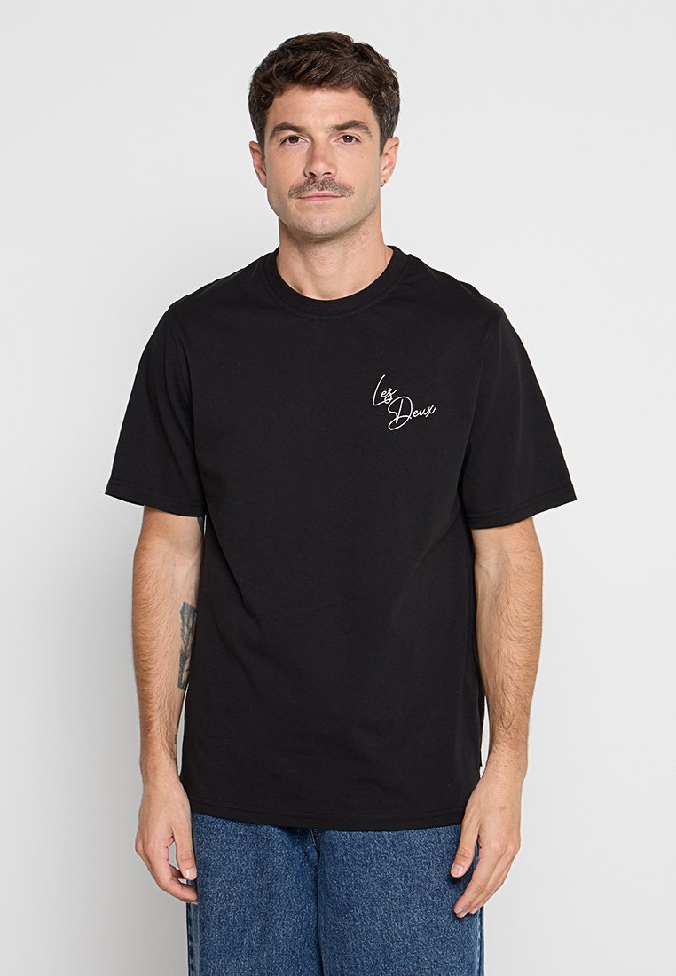Schwarzes Baumwoll-T-Shirt mit lockerer Passform, kurzen Ärmeln und einem weißen, geschwungenen Logo auf der linken Brust. Glatte Textur, simples Design.