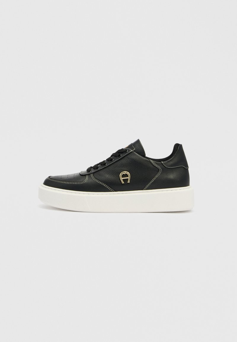 Schwarzer Sneaker aus Leder mit weißer Plateausohle, flachen Schnürsenkeln, goldfarbenem Logodetail und perforiertem Zehenbereich. Glatte Textur mit kontrastierenden Nähten.