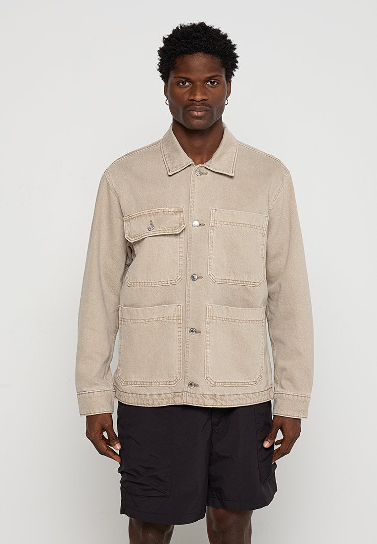 Beige Denimjacke mit Kragen, vier Fronttaschen und silbernen Knöpfen. Sie hat einen lockeren Schnitt und einen strukturierten Stoff.