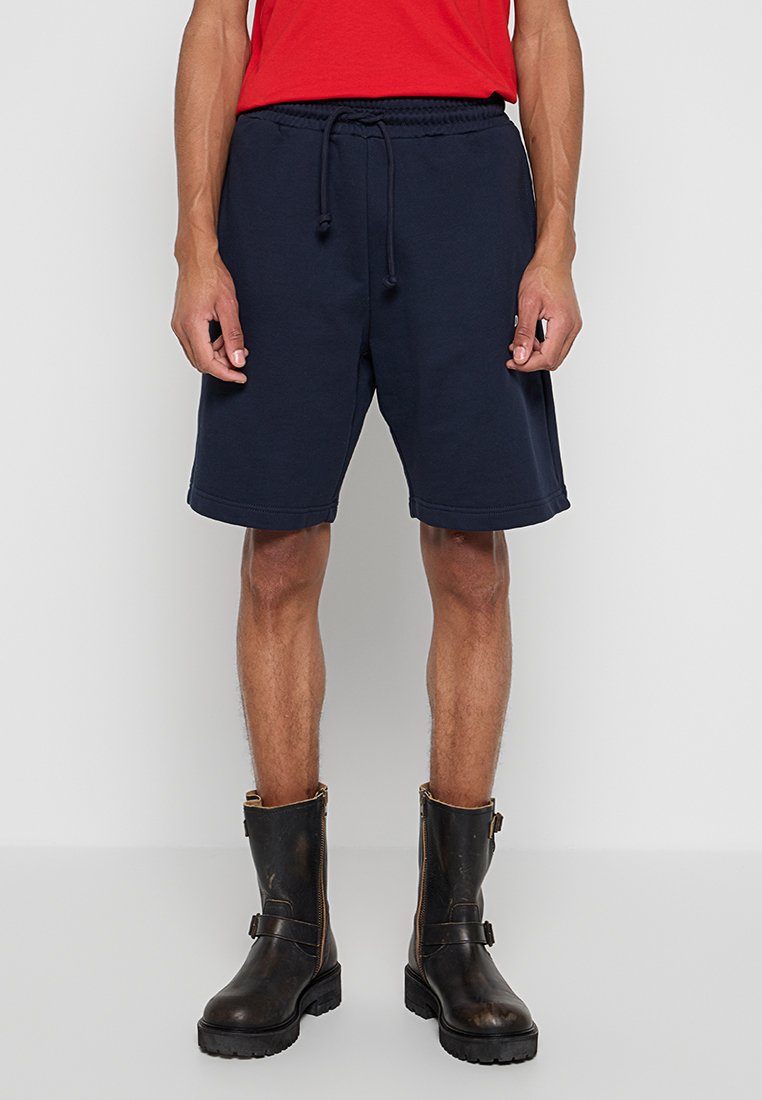 Marineblaue Baumwollshorts mit elastischem Bund, verstellbarem Kordelzug und Seitentaschen. Kombiniert mit braunen Stiefeletten.