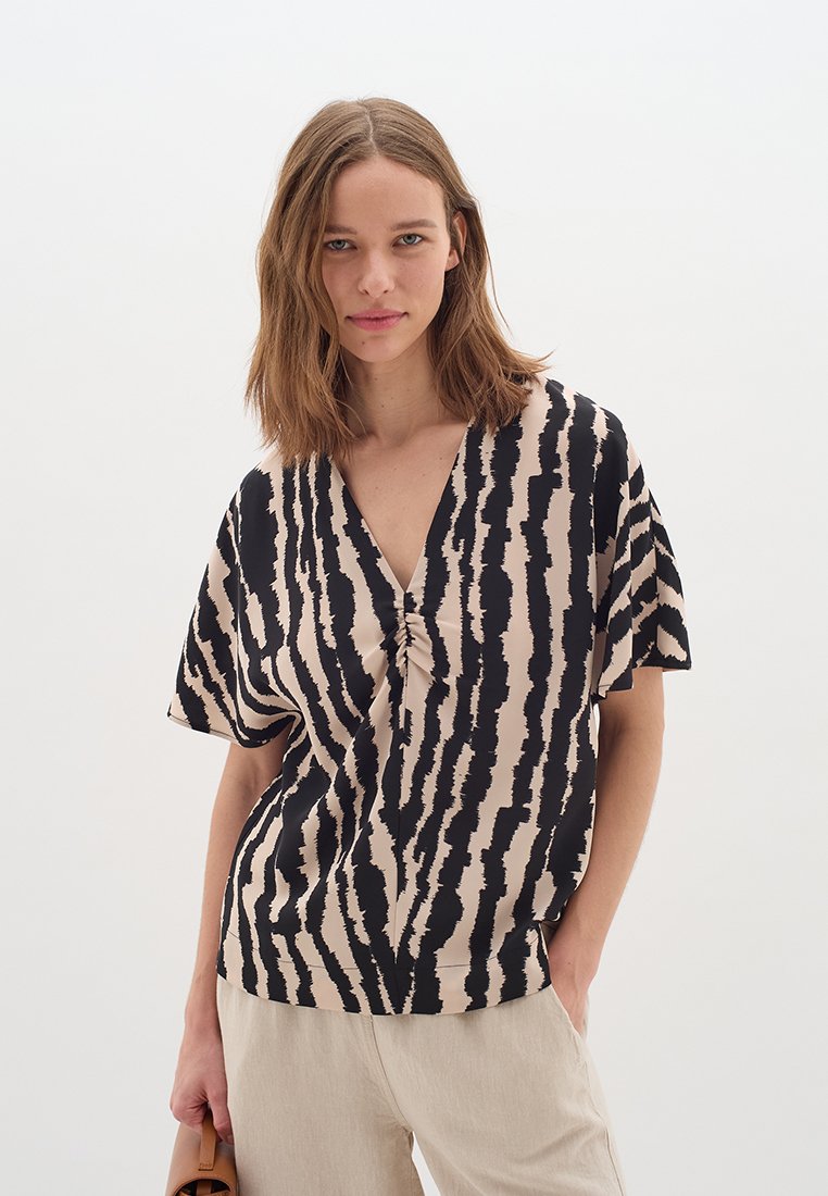 Kurzärmelige Bluse in Beige mit schwarzen vertikalen Streifen, mit V-Ausschnitt und gerafftem Detail an der Vorderseite. Glatte Stofftextur.