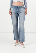 Frau in hellblauen, geraden Jeans mit ausgefranstem Bund, einem kurzen Oberteil und weißen spitzen Kitten-Heels steht.