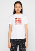 Weißes Baumwoll-T-Shirt mit einem zentralen Grafikdruck eines Sonnenuntergangs über Wasser, mit teilweise sichtbarem Text "DIESEL". Kurze Ärmel, runder Halsausschnitt.