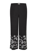 Schwarze Leinenhosen mit weit ausladendem Bein, versehen mit aufwendiger weißer Blumenstickerei am unteren Saum und einem glatten Bund.