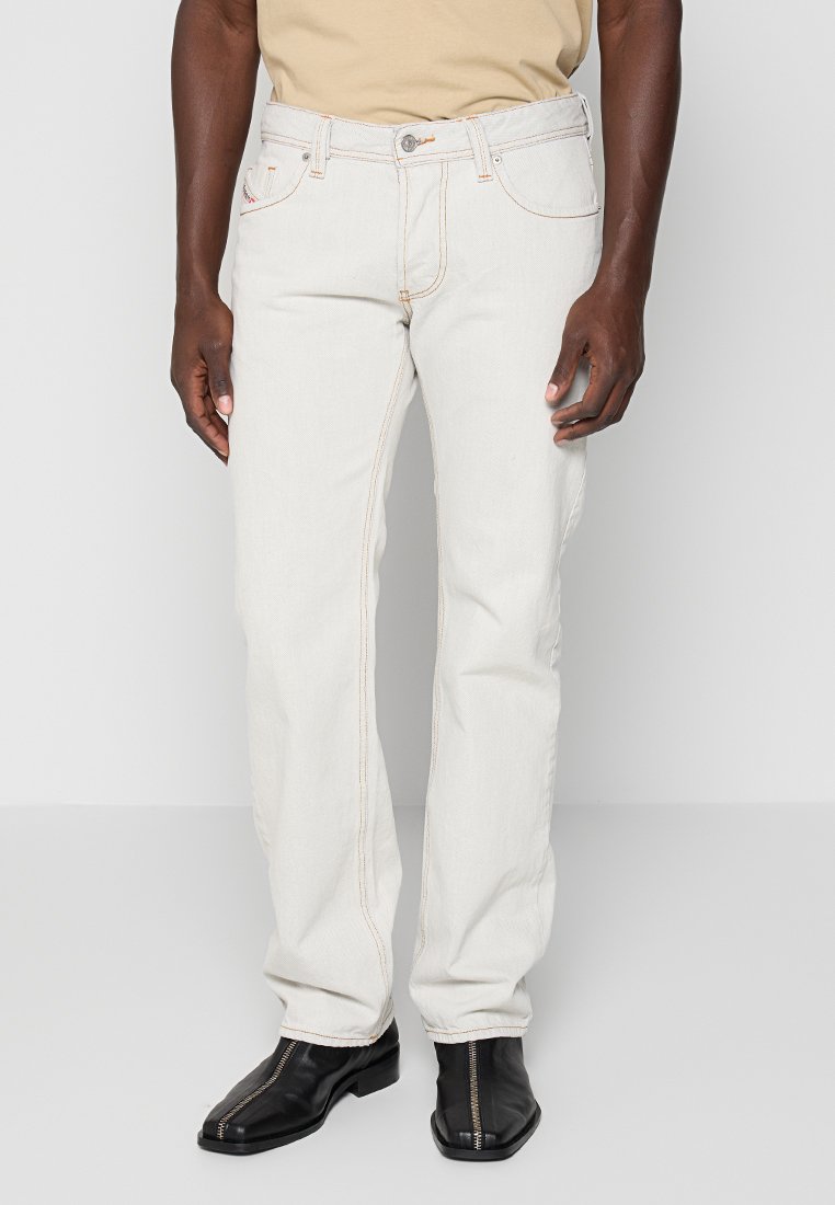 Weiße Jeans aus Denim mit geradem Bein, dezenten orangefarbenen Nähten und klassischem Fünf-Taschen-Design, kombiniert mit schwarzen Stiefeln.
