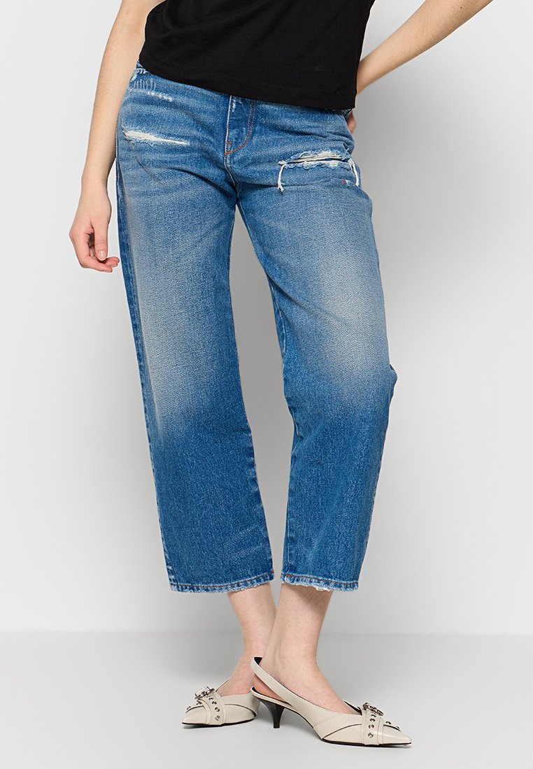 Himmelblaue, mittelhoch geschnittene, cropped Jeans mit fransigen Details. Glatte, denimartige Textur. Kombiniert mit beigen, offenen Heels mit dekorativen Akzenten.