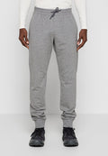 Mann trägt graue Jogginghose mit Kordelzug und Bündchen an den Knöcheln und schwarze Sneakers, steht vor einem hellen, einfachen Hintergrund.