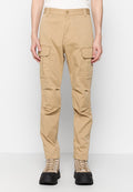 Beige Cargo-Hosen aus Baumwolle mit zwei frontalen Taschen und einer taillierten Passform. Getragen mit beigen Schnürboots und einem schlichten weißen Oberteil.