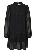 Schwarzes Kleid mit langen transparenten Ärmeln, hohem Kragen und bestickten Details an der Vorderseite und am Saum. Ausgestattet mit einem Rüschensaum.