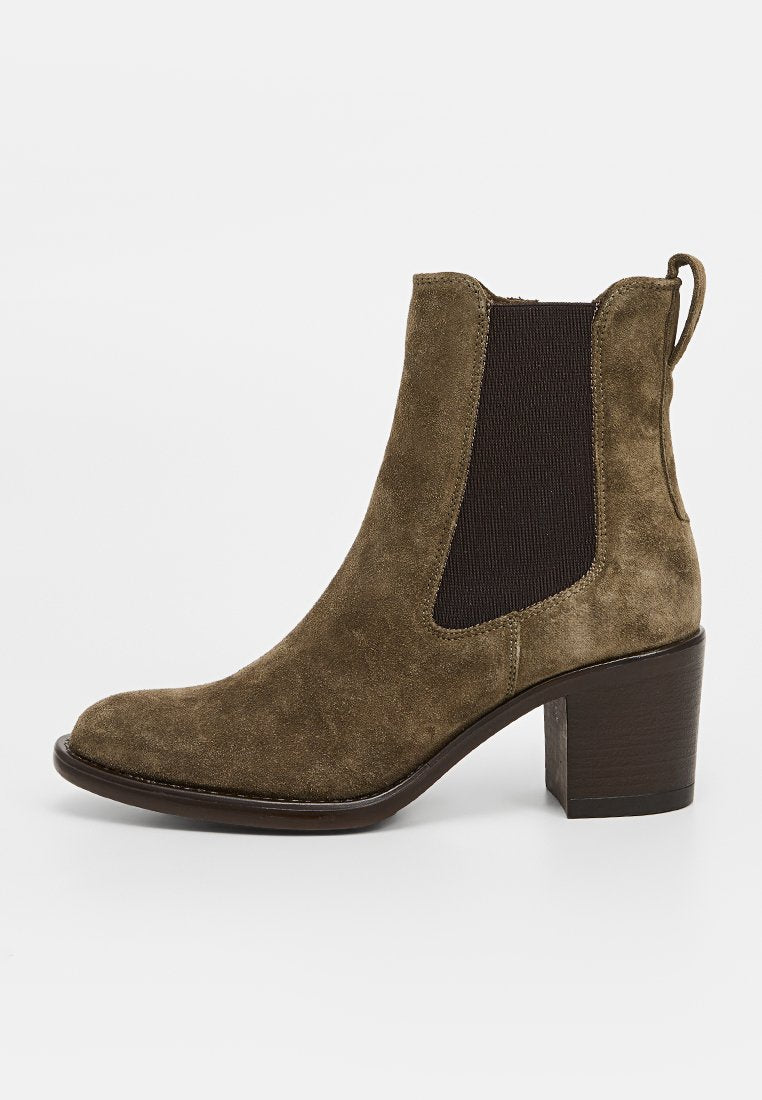 Braune Wildleder Stiefelette mit elastischen Seiteneinsätzen und einer Zuglasche. Der gestapelte Absatz ist ungefähr 5 cm hoch und hat eine runde Zehenform.