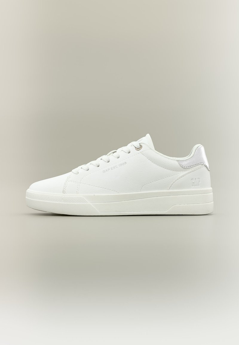 Weißer Sneaker mit niedrigem Schaft, Schnürsenkeln, dezentem Markenlogo an der Seite und Ferse sowie Gummisohle auf neutralem beigem Hintergrund.