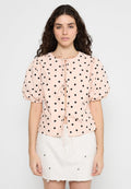 Bluse mit Puffärmeln aus hellpinkem Stoff mit schwarzen Punkten; verfügt über ein Bindeband am Ausschnitt und einen Knopfverschluss.