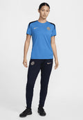 Blaues Sportshirt mit schwarzen Akzenten und Chelsea FC-Logo; kombiniert mit marineblauen Hosen mit Nike-Logo und schmalem Schnitt. Schwarze Sneakers.