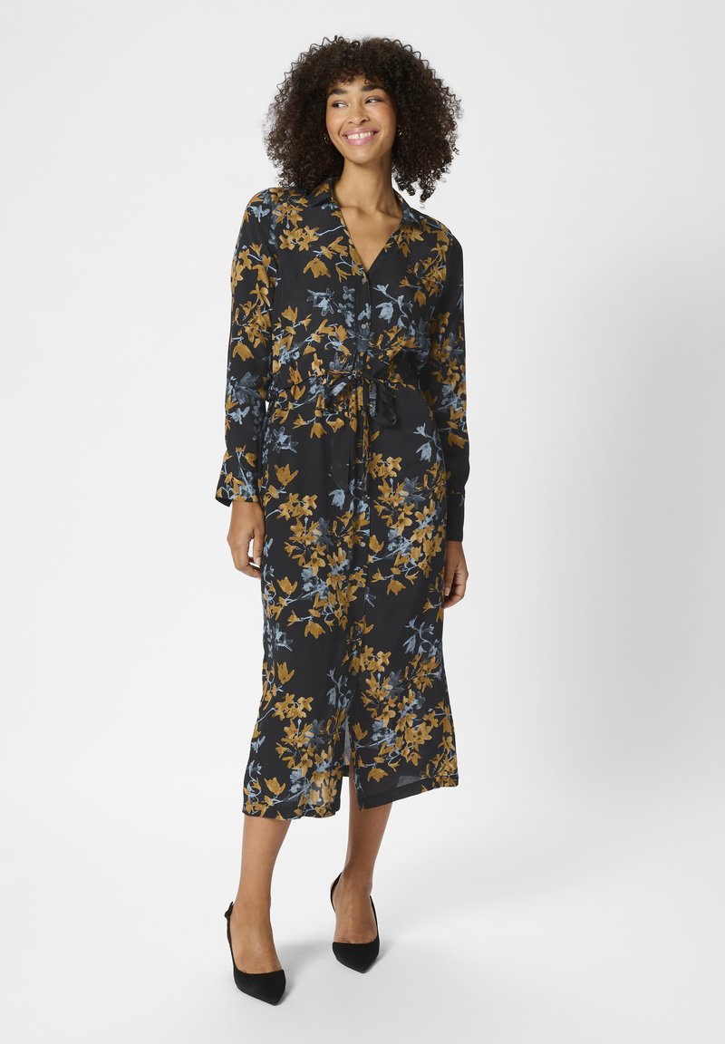 Kleid mit floralem Druck, langen Ärmeln, schwarzer Basis und gelb-blauem Muster. Mit Taillenbindung und mittellangem Saum, weiche Stoffstruktur.