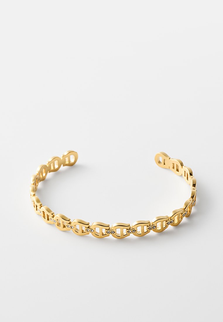 Goldenes offenes Manschettenarmband mit Kettenglieder-Design und kleinen eingesetzten klaren Steinen an jedem Glied, vor weißem Hintergrund.