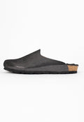 Schwarze Slipper-Clogs mit strukturiertem Obermaterial, Kork-Zwischensohle und schwarzer Gummisohle, seitlich vor weißem Hintergrund dargestellt.