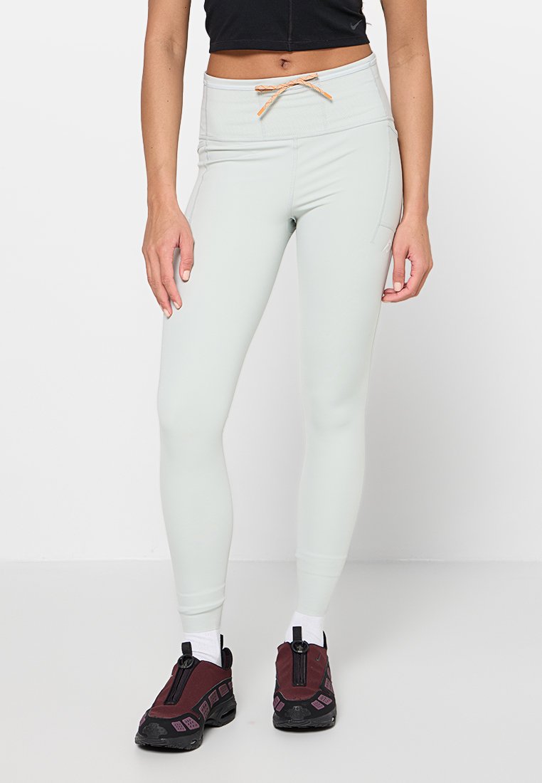 Hellgrüne Leggings mit hohem Bund, Kordelzugdetail und Seitentasche. Kombiniert mit dunkelroten Sportschuhen und weißen Socken.