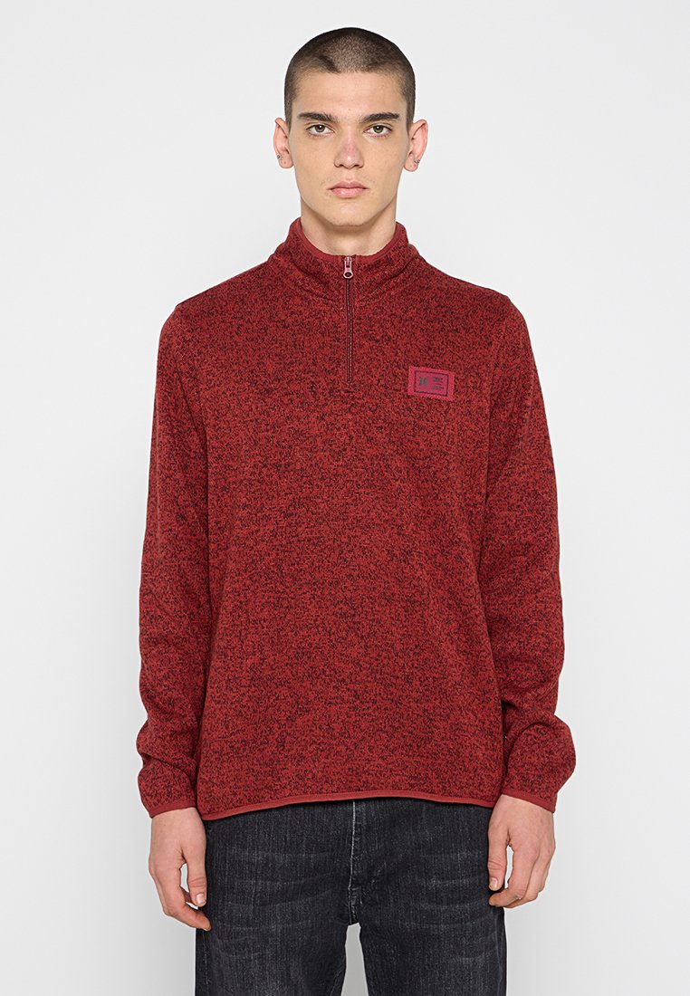 Rot gepunkteter Pullover mit hohem Kragen und Viertelreißverschluss; verfügt über ein kleines Logo-Patch auf der Brust, lange Ärmel und eine lockere Passform.