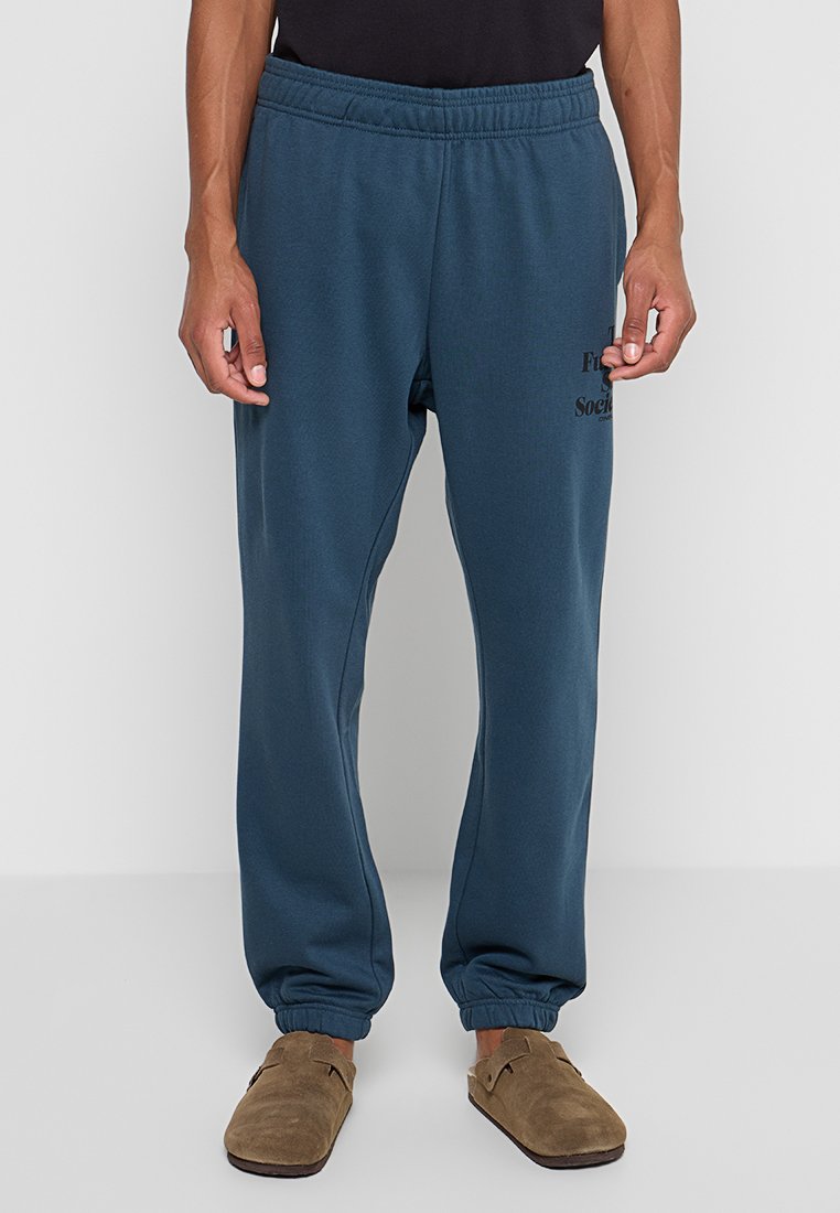 Dunkelblau-grüne Jogginghose aus weichem Material, mit einem elastischen Bund, schmal zulaufenden Bündchen und einem schwarzen Grafikdruck auf dem linken Oberschenkel.