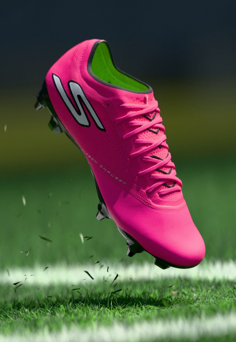 Pinker Fußballschuh mit strukturiertem Obermaterial, schwarzen Akzenten und grünem Innenfutter. Rasensplitter fliegen unter ihm auf, während er über dem Gras schwebt.