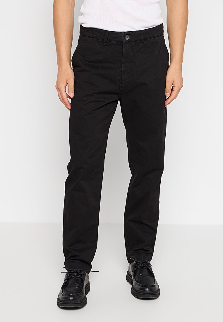 Schwarze Baumwollhosen mit geradem Bein, versehen mit einem Knopfverschluss und Vordertaschen; getragen mit schwarzen Schuhen vor einem weißen Hintergrund.