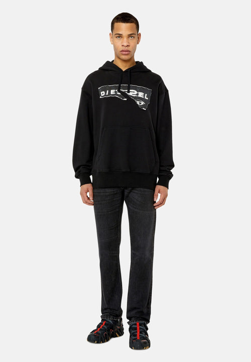 Schwarzes Hoodie mit einem ausgefransten weißen Logo, Kängurutasche, gerippte Bündchen, kombiniert mit dunklen Jeans und schwarzen Schuhen mit roten Akzenten.