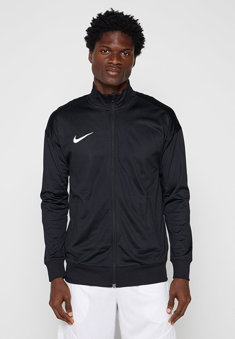 Mann trägt eine schwarze Nike-Sportjacke mit Reißverschluss und weiße Sportshorts, steht vor einem schlichten Hintergrund.