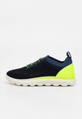 Navyblauer und neongelber Sneaker mit gestricktem Obermaterial, gepolsterter weißer Sohle und gemusterten Schnürsenkeln, von der Seite auf einfarbigem Hintergrund dargestellt.