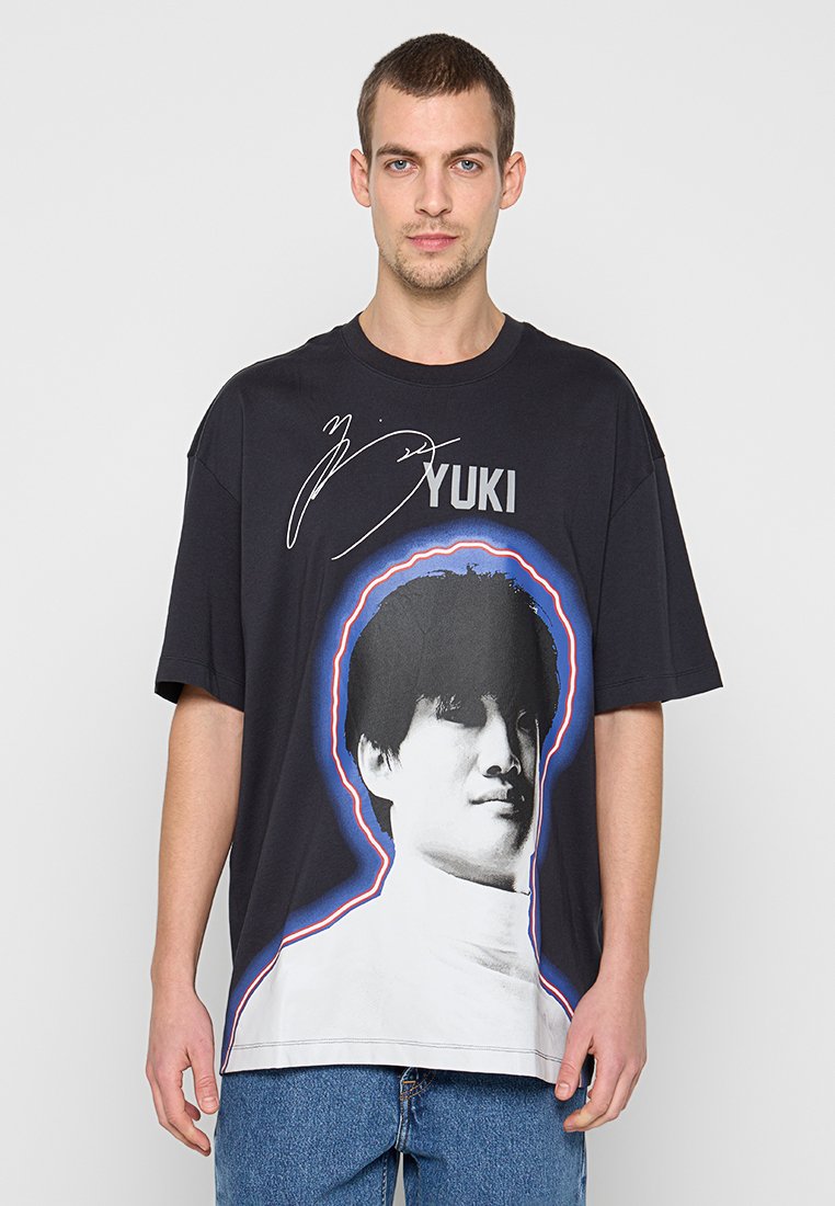 Schwarzes Baumwoll-T-Shirt mit großem Grafikdruck eines menschlichen Gesichts, umrandet mit blauen und roten Akzenten. Locker geschnittenes Design.