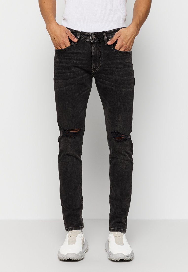 Schwarze Jeans aus Denim mit schmaler Passform, die abgenutzte Knie-Risse, fünf Taschen und einen Knopfverschluss aufweist. Kombiniert mit weißen Sneakers.