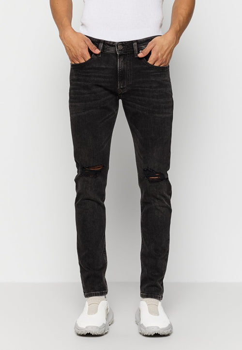 Schwarze Jeans aus Denim mit schmaler Passform, die abgenutzte Knie-Risse, fünf Taschen und einen Knopfverschluss aufweist. Kombiniert mit weißen Sneakers.