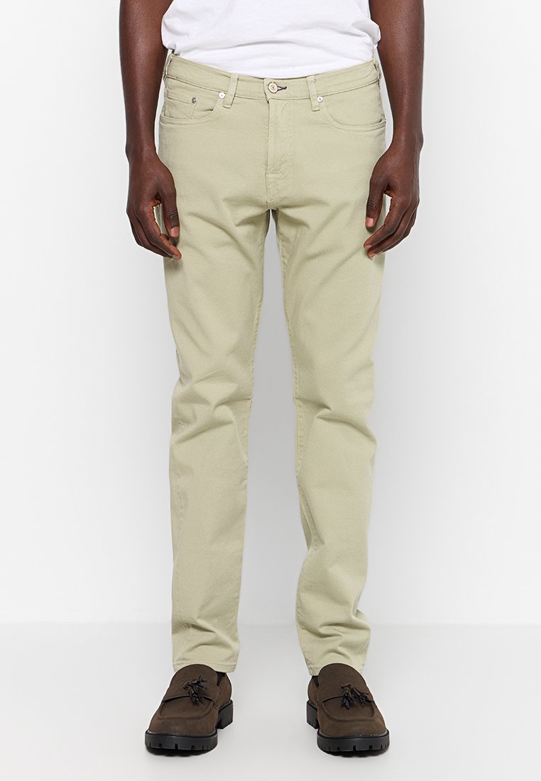 Beige Chinos mit schmaler Passform, ausgestattet mit einem Knopf- und Reißverschluss, fünf Taschen und dezenten Nähdetails. Kombiniert mit dunklen Schuhen.