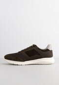 Dunkelbraune Sneaker mit einem Obermaterial aus Mesh und Wildleder, weißer strukturierten Gummisohle und einem weißen gepolsterten Kragen vor einem schlichten hellen Hintergrund.
