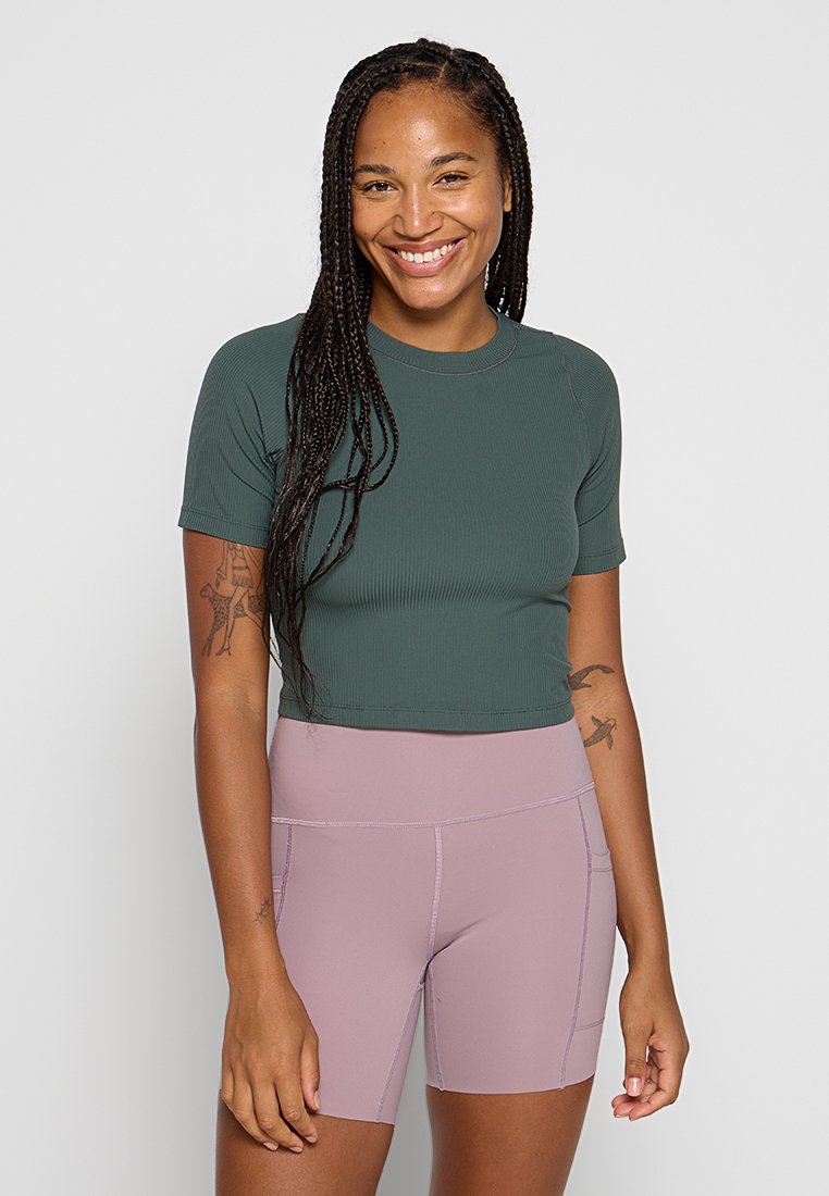 Dunkelgrünes, geripptes, kurzärmeliges Croptop, kombiniert mit hellrosa, hochtaillierten Radshorts mit kontrastierenden Nähten und kleinen Taschen.