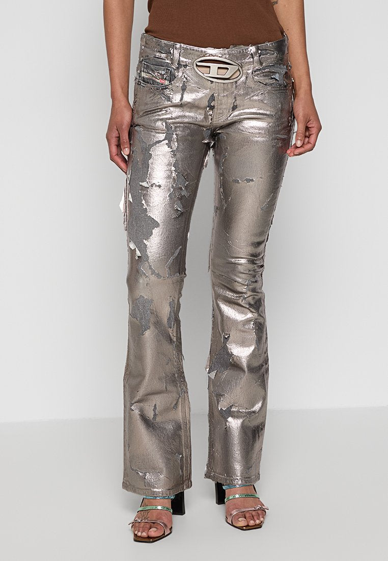 Metallisch silberne Schlagjeans mit distressed Textur und gemusterten Details. Verfügt über Fronttaschen und eine auffällige Gürtelschnalle.