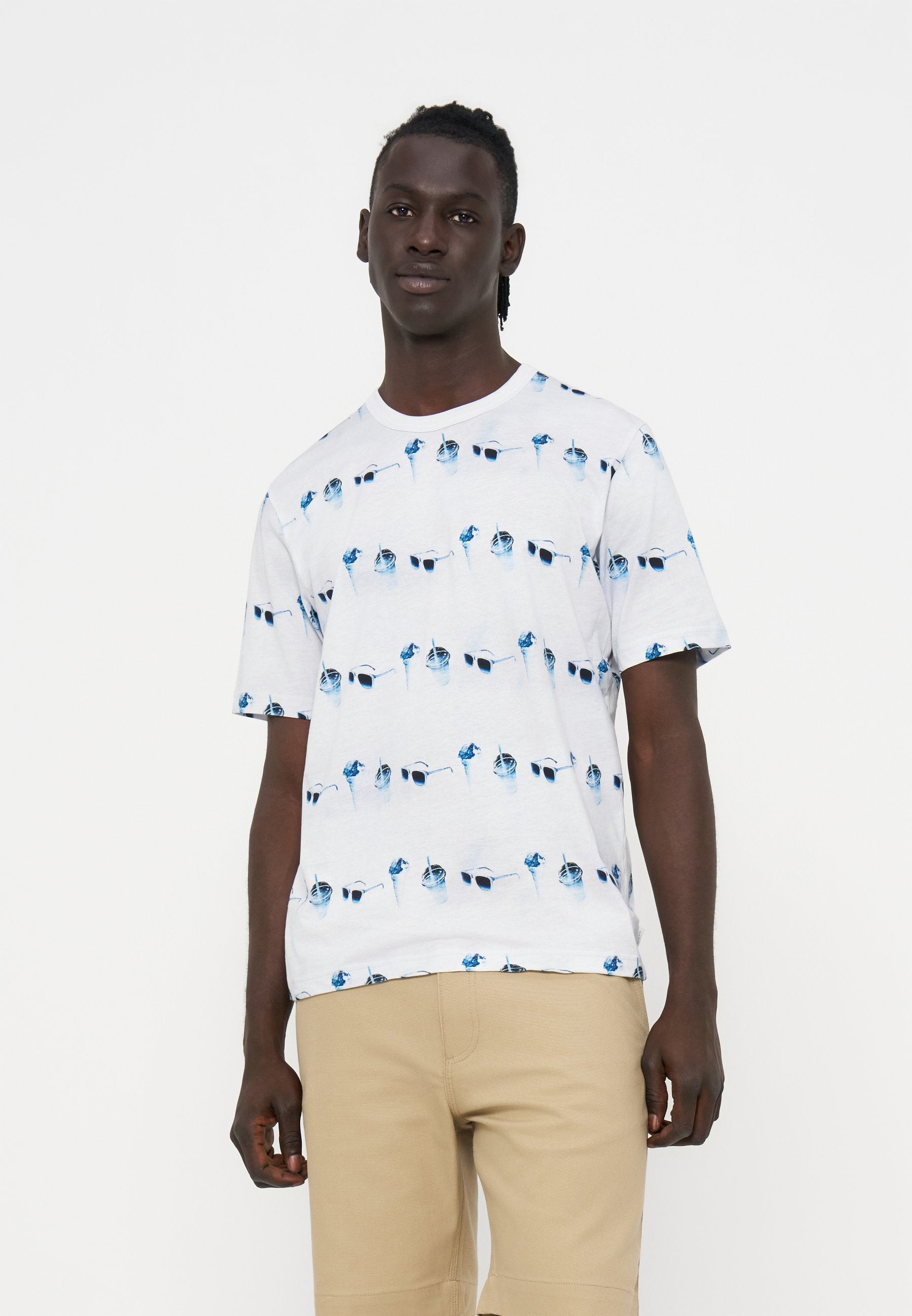 Mann trägt ein weißes kurzärmliges T-Shirt mit einem blauen Sonnenbrillen- und Getränke-Muster und beigen Shorts auf weißem Hintergrund.